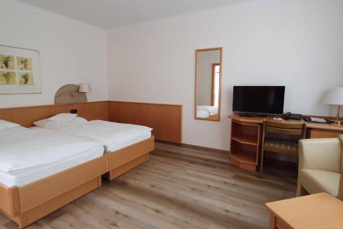 A hotel room with two single beds, a desk with a television, a chair, and a small table.
