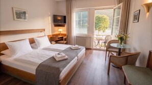 A hotel room with a bed, a desk, a chair, a TV, and a balcony with a table and chairs. - Hotel Schön (Ruedesheim am Rhein)