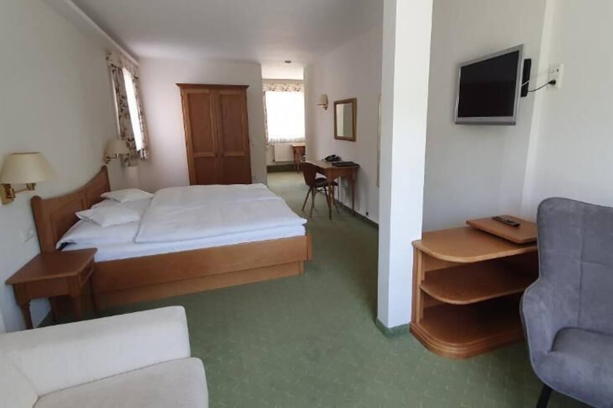 A hotel room with a bed, a desk, a chair, a TV, and a wardrobe.