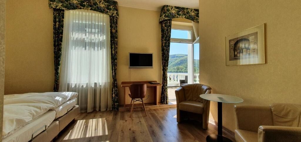 A hotel room with a bed, a desk, a chair, a small table, and a TV.