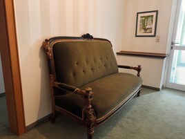 Un sofá de estilo vintage con patas de madera ornamentadas y un respaldo acolchado, situado frente a una pared con diseño a rayas.