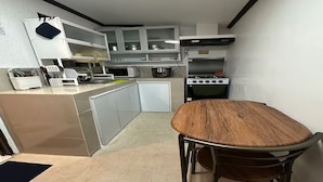 A compact kitchen with a dining table, cabinets, a microwave, a stove, and a sink.