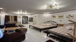 A modern hotel room with two beds, a sofa, a desk, and a fan.
