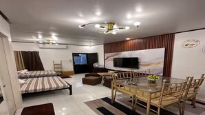 A modern living room with a sofa, a dining table with chairs, a flat-screen TV, and a ceiling light fixture.