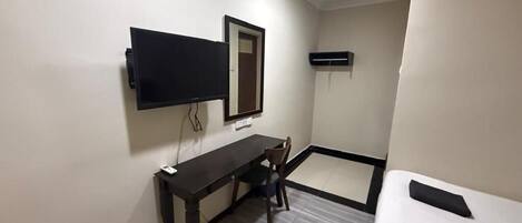 Habitación de hotel con cama, escritorio, silla, televisor de pantalla plana montado en la pared y equipo de aire acondicionado.