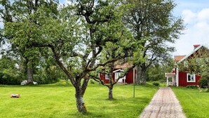 A gravel path leading to a red building with a white door, surrounded by lush green grass and trees. - 4 Person Holiday Home in Aneby (Aneby)