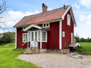Ein rotes Holzhaus mit geneigtem Dach und einer Veranda.