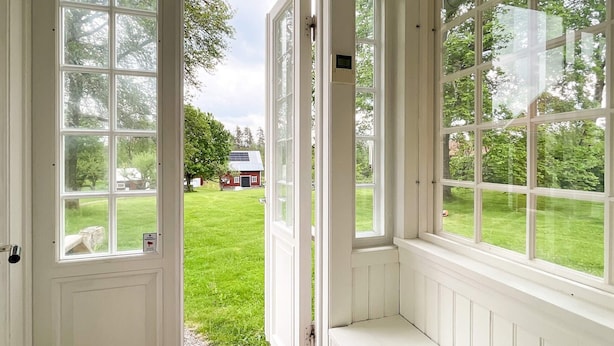A conservatory with large windows, a bench, and a view of a grassy yard and a red building. - 4 Person Holiday Home in Aneby (Aneby)