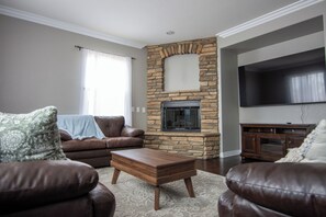 A living room with a stone fireplace, leather sofas, a wooden coffee table, and a flat-screen TV mounted on the wall. - Beautiful 4 Bedroom - Fun Family Pet Friendly Home (Lancaster)