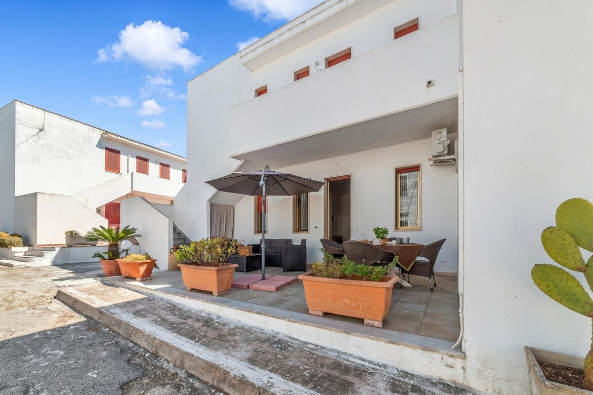A white building with a patio area featuring outdoor furniture, potted plants, and a cactus.