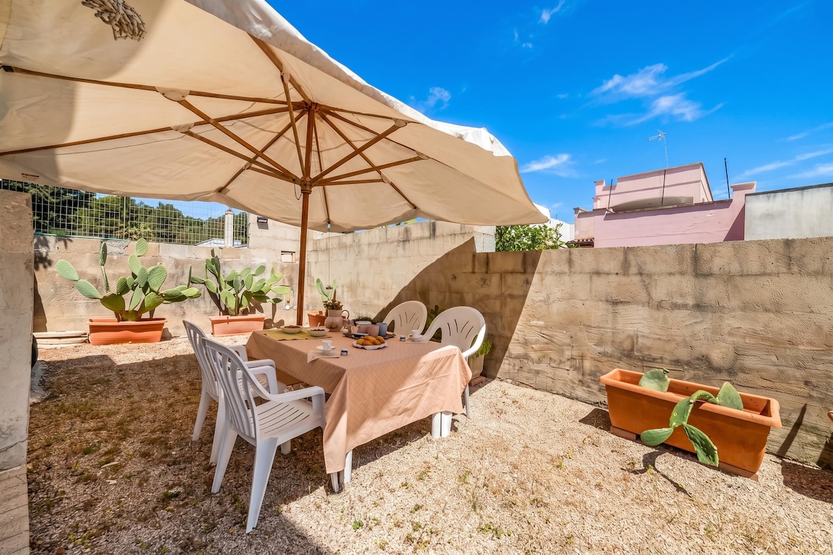 An outdoor patio with a table and chairs under a large umbrella, surrounded by potted cacti.
