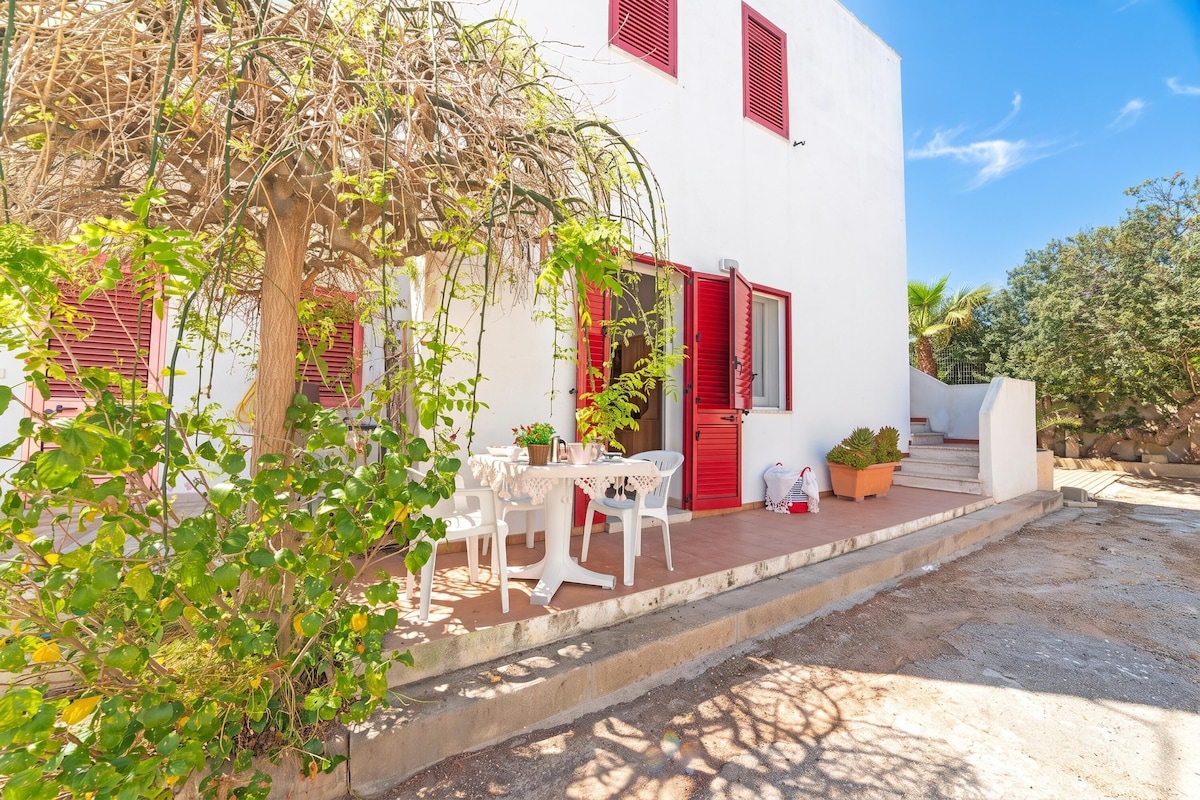 A white building with red shutters, a table with chairs, and potted plants.
