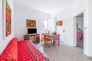 A room with a bed, a desk, a chair, a table with a bowl of fruit, and a television. - Leuca Relax And Sea Apartments (Castrignano del Capo)