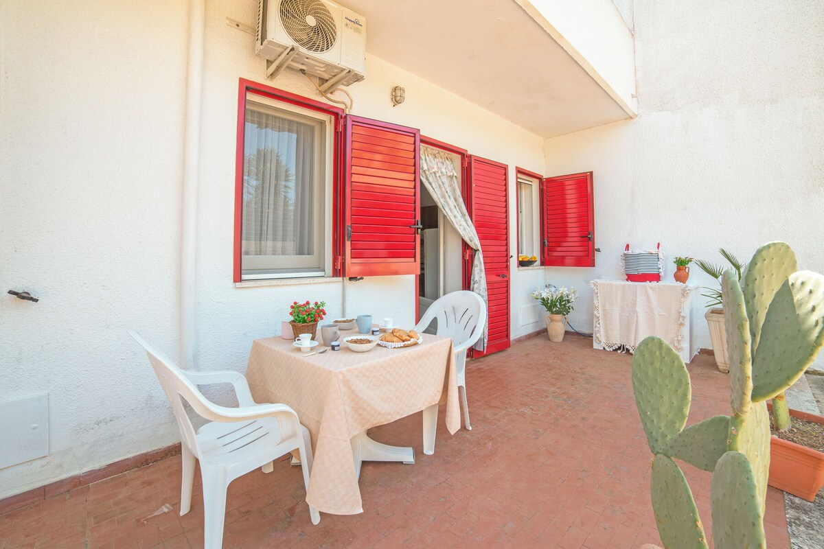 A patio with a table set for two, red shutters, a cactus plant, and a white chair.