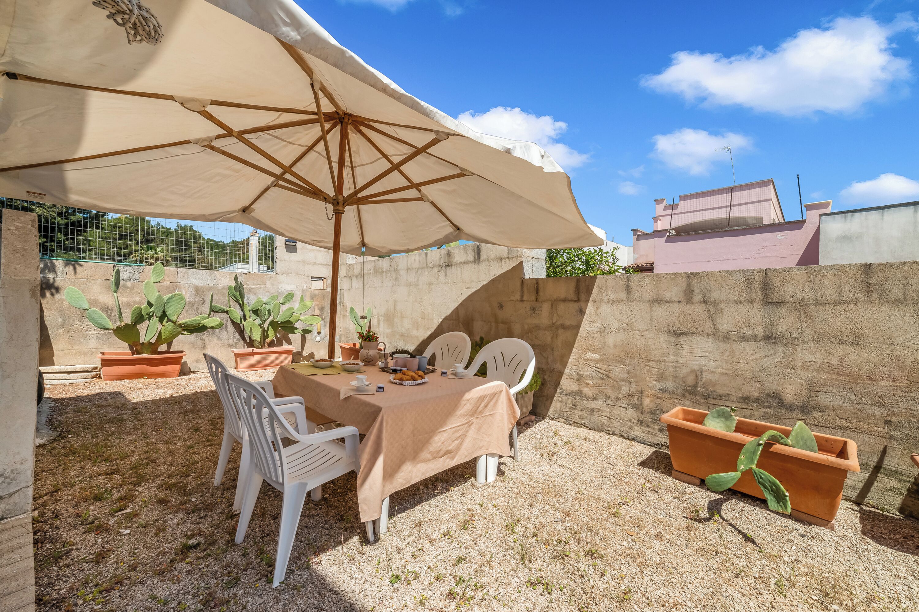 Eine Terrasse im Freien mit Tisch, Stühlen, einem großen Sonnenschirm und Blumentöpfen.