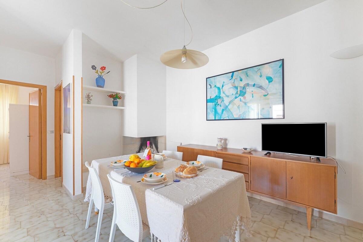 A dining area with a table set for two, a television, and a painting on the wall.