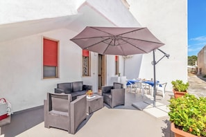 A patio area with outdoor furniture, a large umbrella, and potted plants. - Leuca Relax And Sea Apartments (Castrignano del Capo)