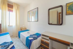Ein Hotelzimmer mit zwei Betten, einem Schreibtisch, einem Schminktisch, einem Fenster mit Vorhängen, einer Karte an der Wand und einem Spiegel.