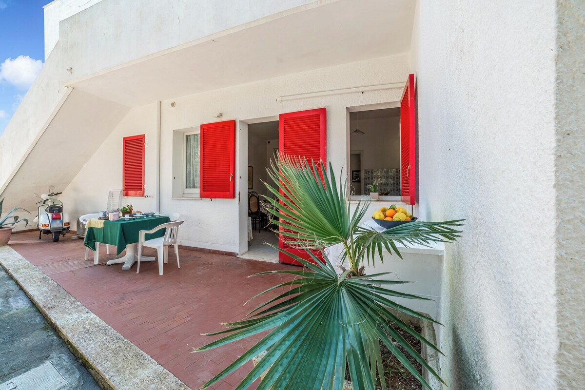 A white building with red shutters, a table with chairs, and a potted plant.