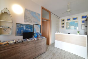 Ein Empfangsbereich mit einem Holztisch, einem Fernseher, gerahmten Karten und einem Deckenventilator.