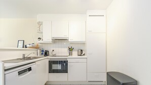 Eine kompakte Küche mit weißen Schränken, einem Geschirrspüler, einem Backofen und einem Mülleimer.