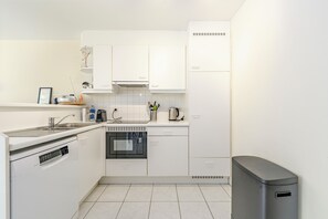 Eine kompakte Küche mit weißen Schränken, einem Geschirrspüler, einem Backofen und einem Mülleimer.