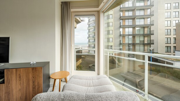 Ein modernes Hotelzimmer mit großem Fenster, einem Flachbildfernseher, einem Holzschrank und einem Sofa.