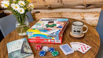 Ett Monopolyspel upplagt på ett träbord, tillsammans med en bok, pokermarker, spelkort, en mugg och en vas med blommor.