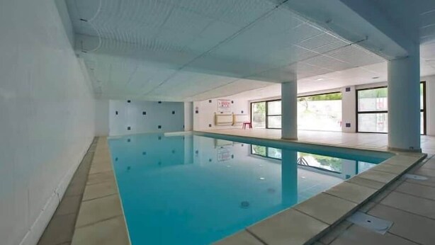 An indoor swimming pool with clear water, tiled floor, and large windows. - 10 des Oliviers | 2 min from downtown Uzès | pool + AC + parking (Uzès)