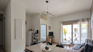 A modern living room with a dining area, a TV, and a large window. - 10 des Oliviers | 2 min from downtown Uzès | pool + AC + parking (Uzès)