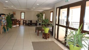 A lobby with a reception desk, seating area, potted plants, and a large window. - 10 des Oliviers | 2 min from downtown Uzès | pool + AC + parking (Uzès)