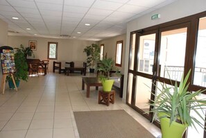 Eine Lobby mit Empfangstresen, Sitzgelegenheit, Zimmerpflanzen und einem großen Fenster.