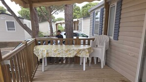 A covered deck with a table and chairs, a wooden railing, and a view of a residential area. - Air-conditioned mobile home for 6–8 people—direct beach access at a 4-star comfort campground (Canet-en-Roussillon)