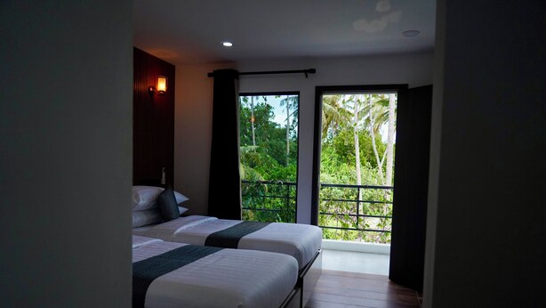 Habitación de hotel con dos camas, una ventana con vista a la vegetación y una lámpara en el techo.
