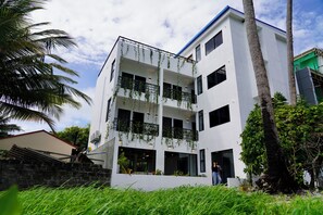 Un edificio de varios pisos con balcones, rodeado de follaje y palmeras.