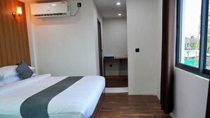 Una habitación de hotel con cama, aire acondicionado instalado en la pared, ventana con cortinas y piso de madera.