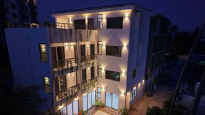 Un edificio de varios pisos con balcones, ventanas amplias y mesas al aire libre.