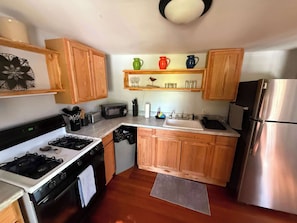 Una cocina compacta con armarios de madera, un refrigerador de acero inoxidable, un microondas, una estufa y un lavamanos.