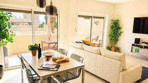 A modern living room with a sofa, dining table, and a TV. - Modern Apartment with Pool Steps from the Beach (Lagos)
