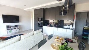 Een moderne woonkamer met een bank, een eettafel met eten en een keuken met kasten en apparatuur.