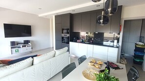 A modern living room with a sofa, a dining table with food, and a kitchen area with cabinets and appliances. - Modern Apartment with Pool Steps from the Beach (Lagos)