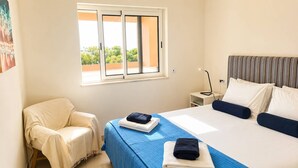 Een slaapkamer met een bed, een stoel, een nachtkastje en een raam met uitzicht.