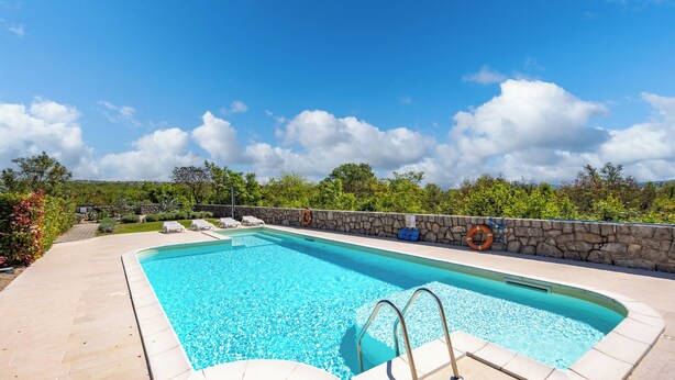 Una piscina rettangolare con una parete in pietra e un cielo azzurro limpido.