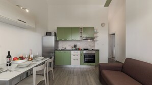 Una cucina compatta con mobili verdi, un piano di lavoro bianco e un divano marrone.