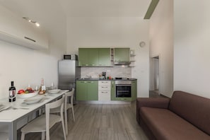 Een kleine keuken met groene kastjes, een wit aanrecht en een bruine bank.