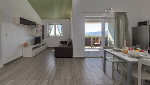 A modern living space with a sofa, TV, dining table, and a balcony with a view. - Wabi Sabi Apartment 3 (Krk)