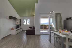 Ein stilvolles Wohnzimmer mit Sofa, Fernseher, Esstisch und einem Balkon mit Blick.