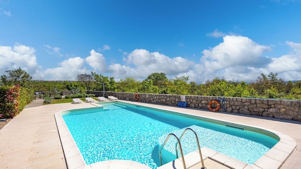 A rectangular swimming pool with a stone wall and a clear blue sky. - Wabi Sabi Apartment 3 (Krk)