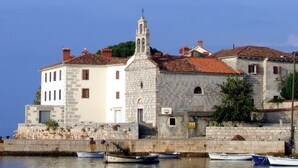 A coastal building with a bell tower, stone walls, and a waterfront with boats. - Wabi Sabi Apartment 3 (Krk)