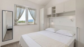 A bedroom with a bed, a window with curtains, a mirror, and built-in shelving. - Wabi Sabi Apartment 3 (Krk)